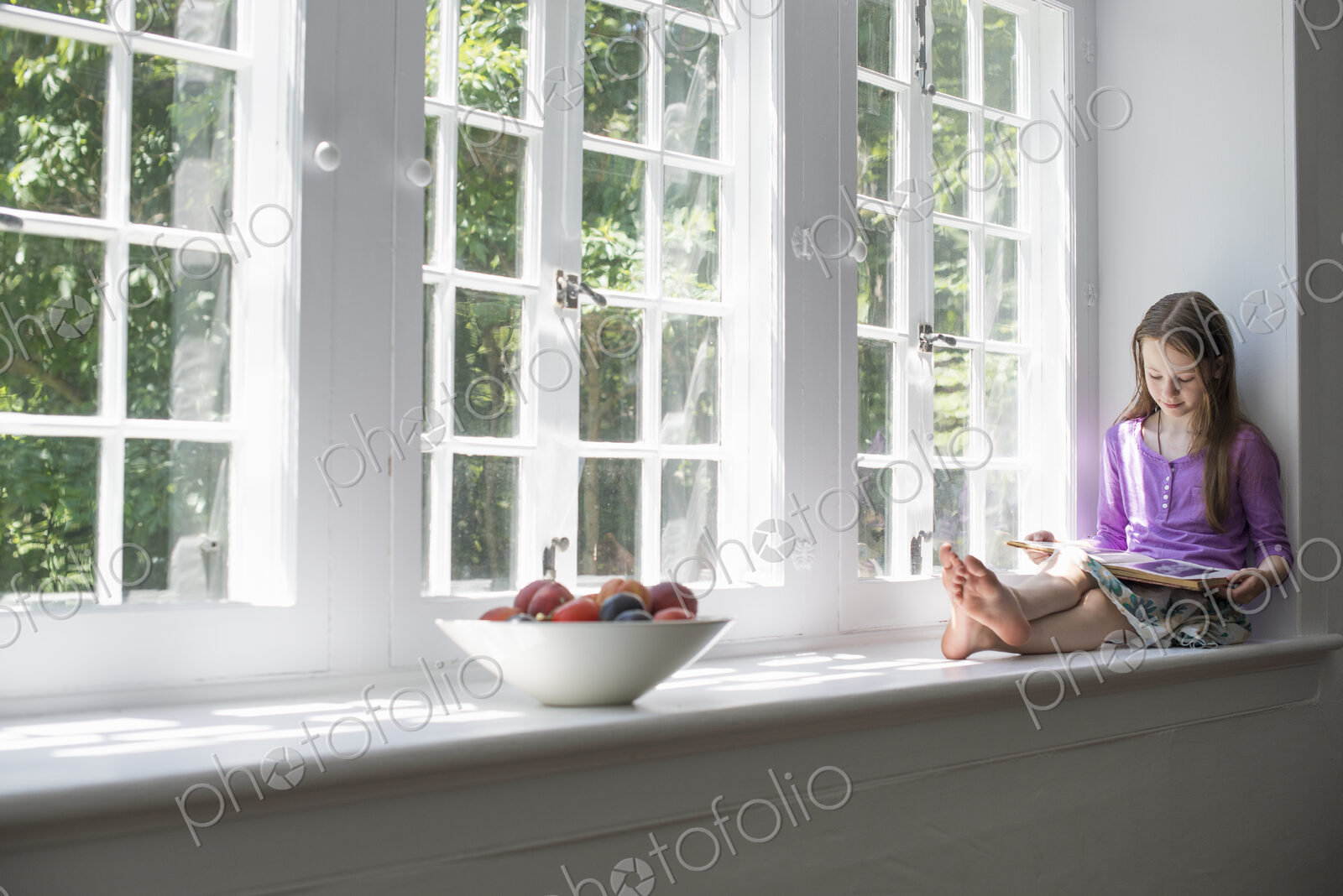 Girl sitting by a window, reading a book.