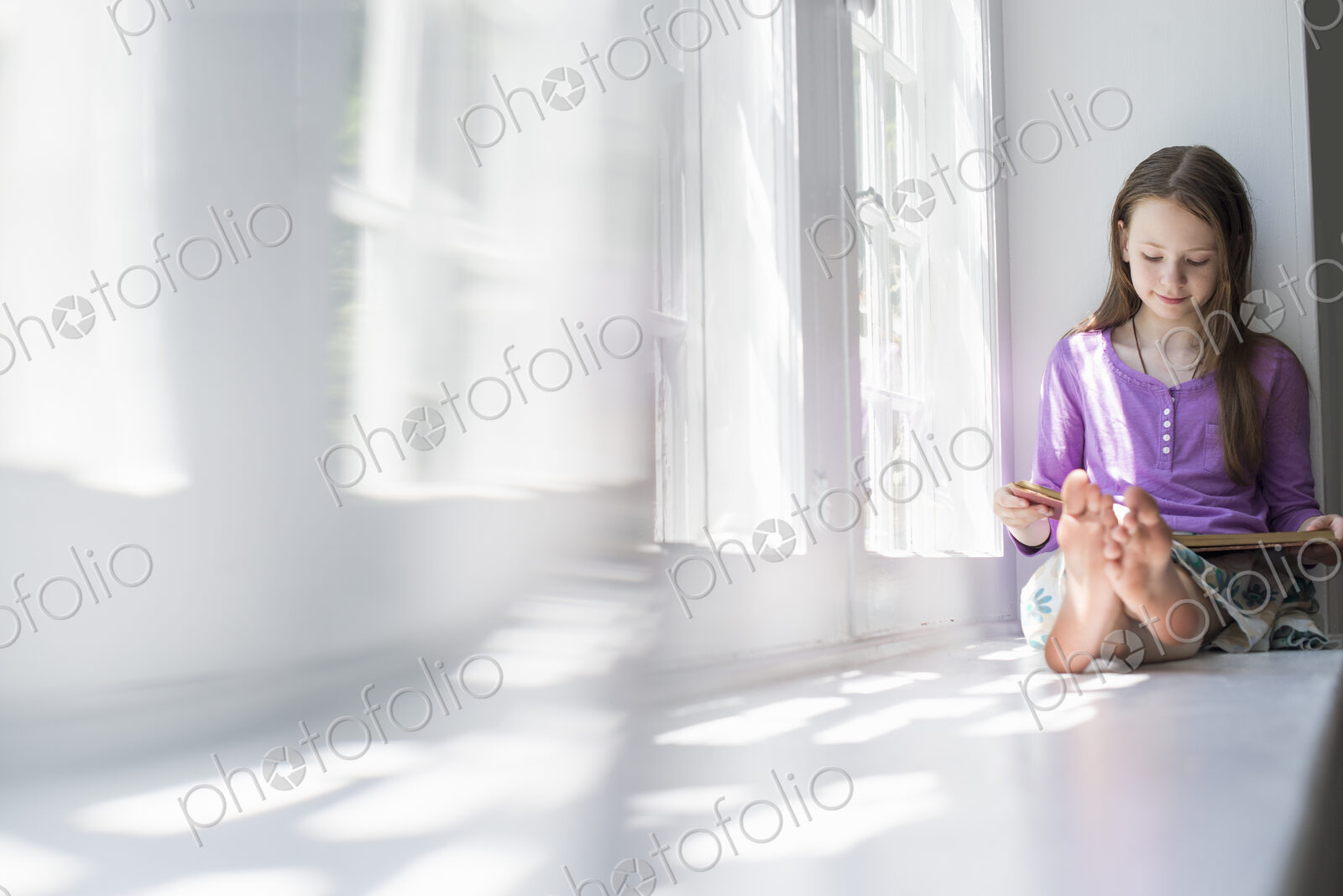 Girl sitting by a window, reading a book.