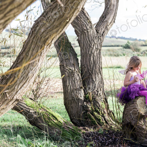 Girl sitting in tree with rural landscape beyond.