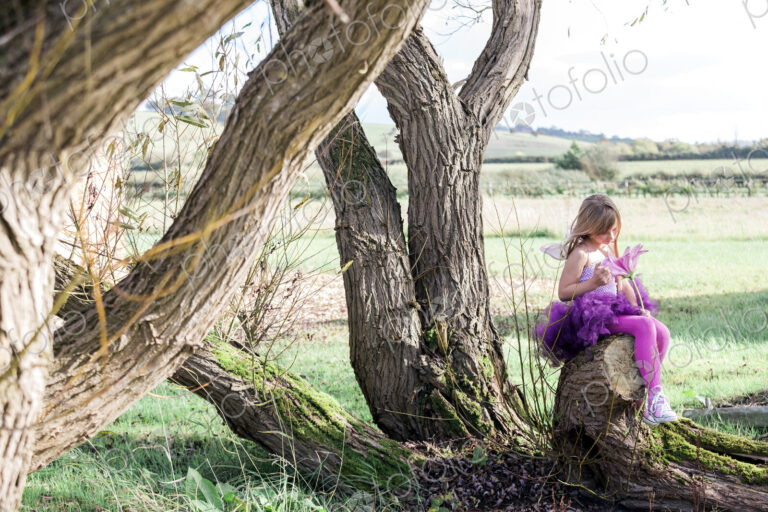 Girl sitting in tree with rural landscape beyond.