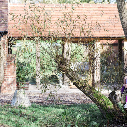 Girl sitting on tree in garden outside house.