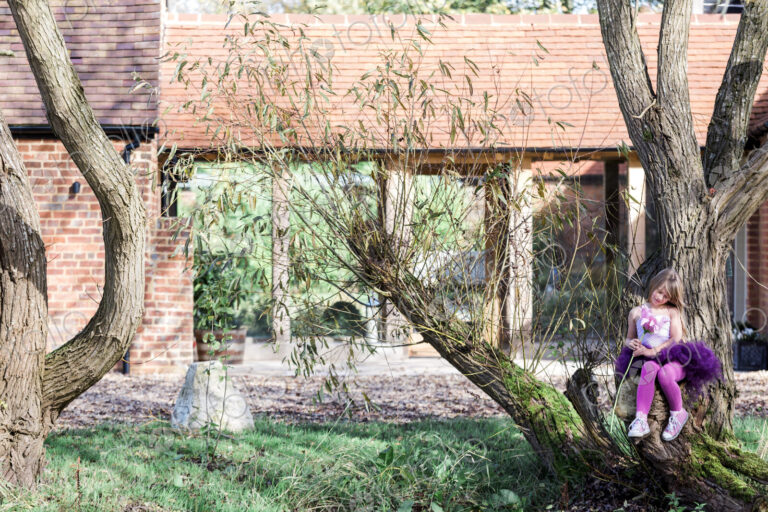 Girl sitting on tree in garden outside house.