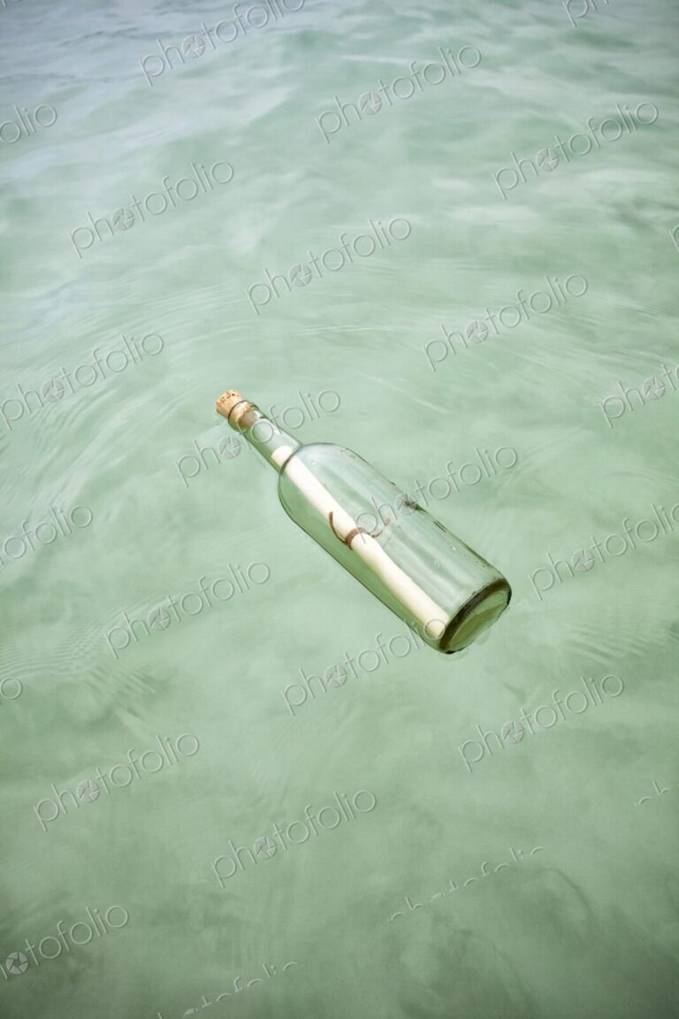 Glass bottle with a rolled note floats on clear Caribbean water. Concept of mystery,…