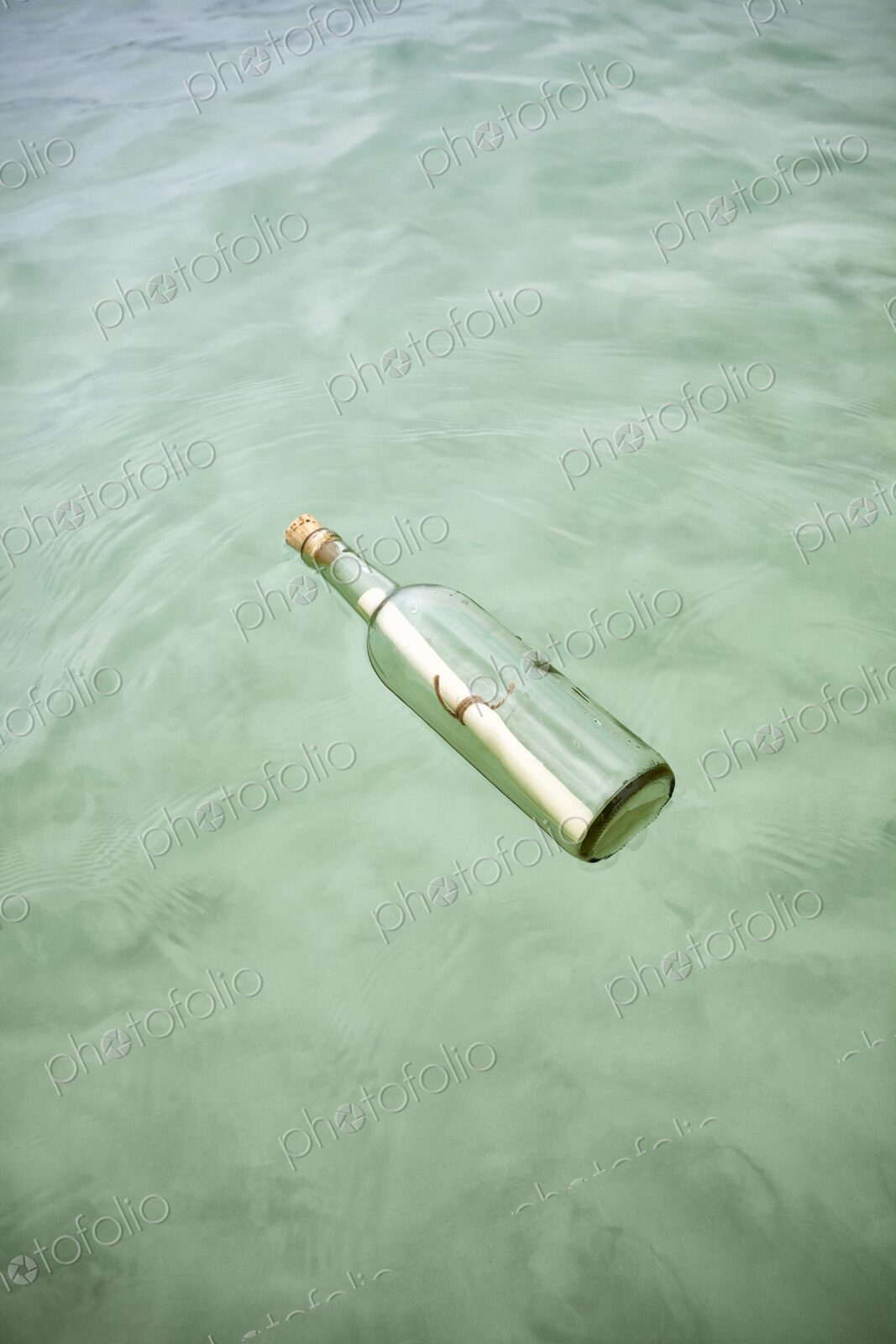 Glass bottle with a rolled note floats on clear Caribbean water. Concept of mystery,…