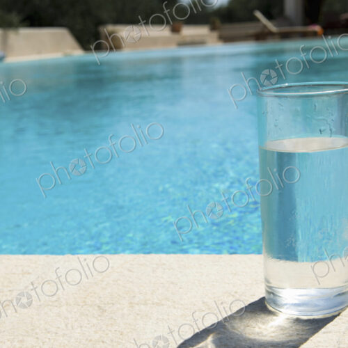 Glass of water on the side of a swimming pool