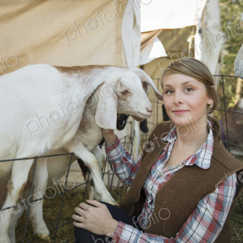 Goats in a pen leaning over the fences at a farm. A young woman tickling the chin of a… Goats in a pen leaning over the fences at a farm. A young woman tickling the chin of a…