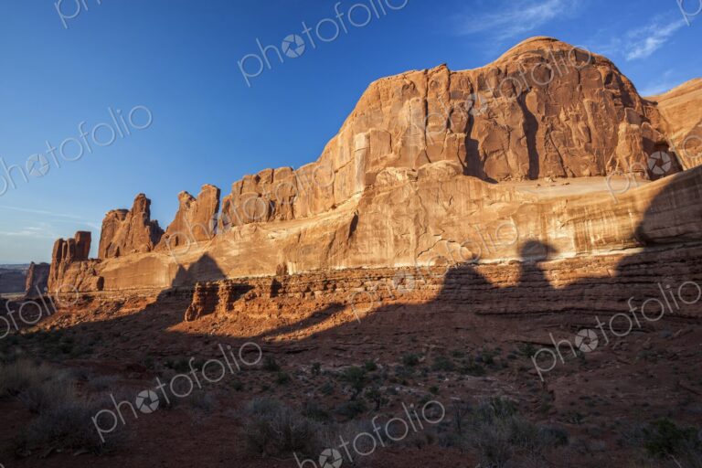 Golden evening light illuminates the towering sandstone cliffs of the Park Avenue rock…