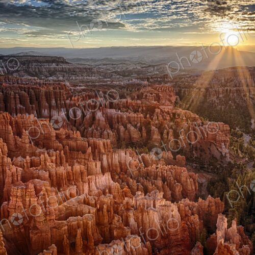 Golden sunbeams pierce the horizon at Bryce Canyon, casting dramatic light over the…