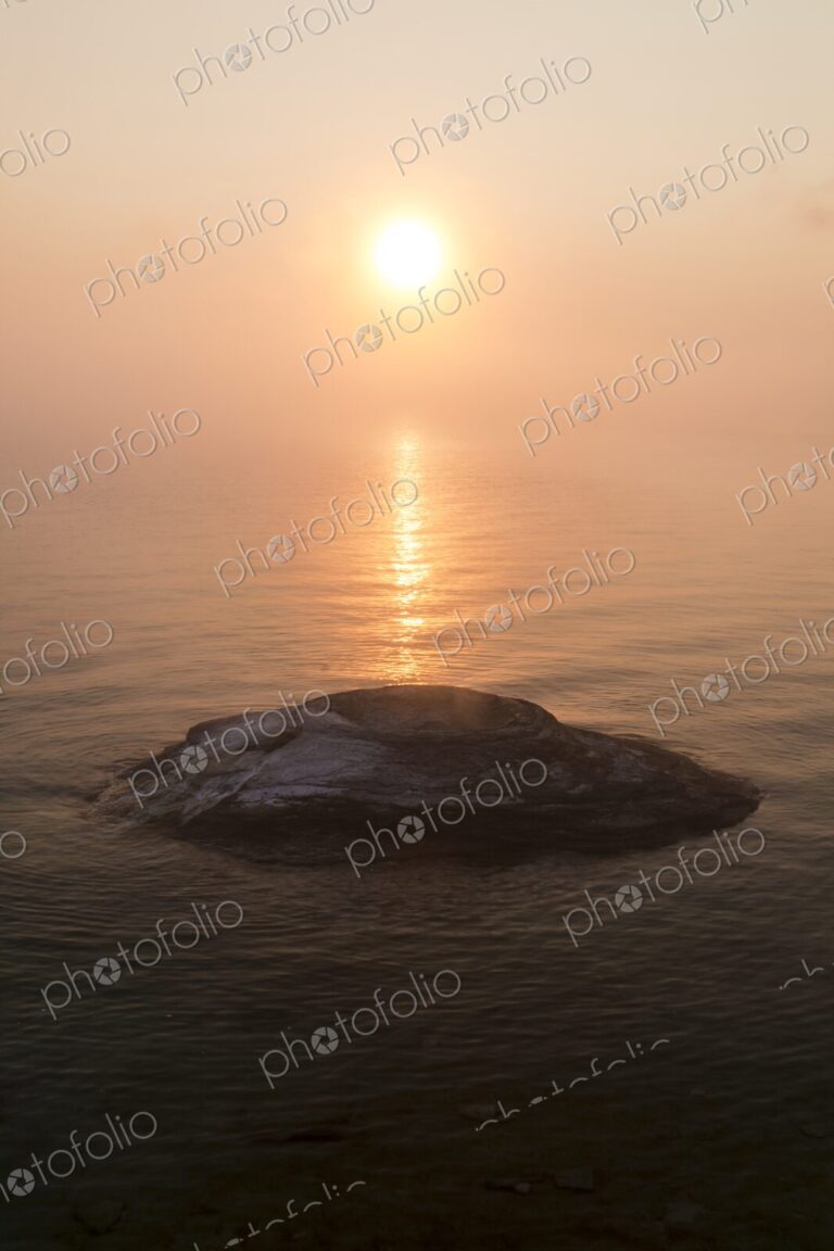 Golden sunrise over Yellowstone Lake with Fishing Cone hot spring emerging from the…