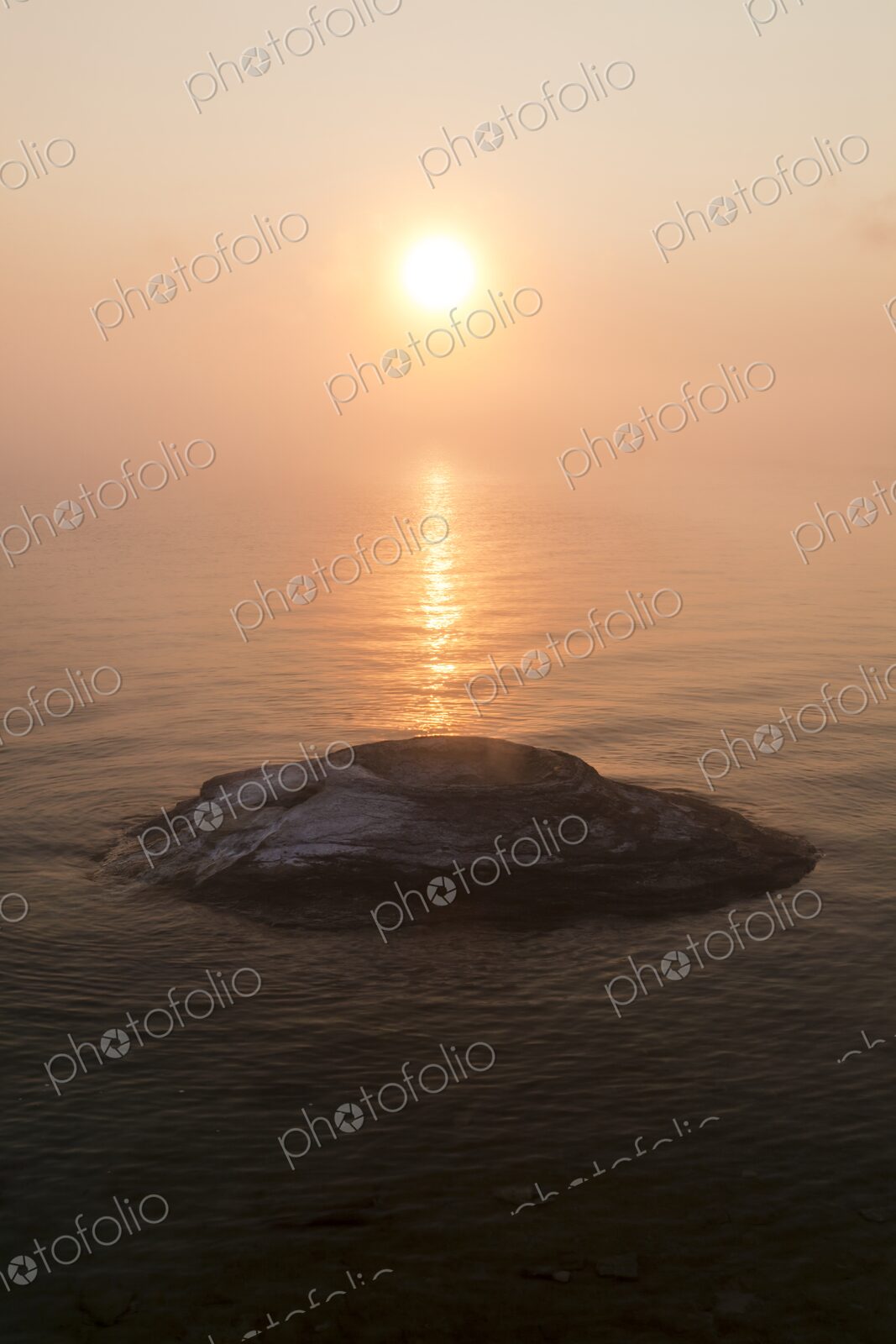 Golden sunrise over Yellowstone Lake with Fishing Cone hot spring emerging from the…
