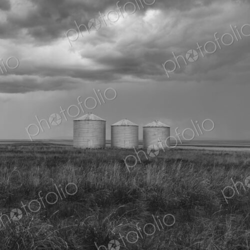Grain silos and storm clouds over vast areas of farmland and prairie.