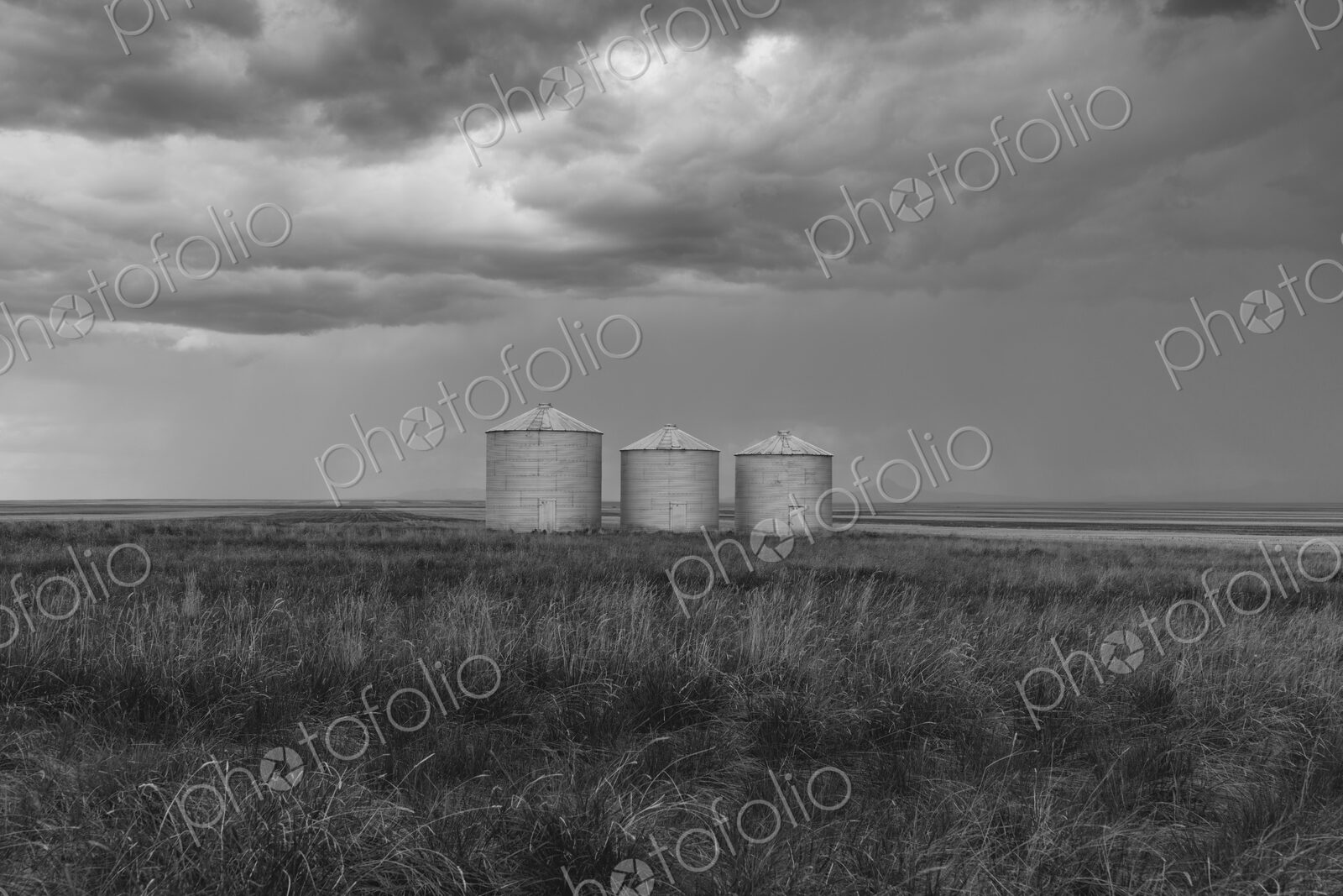 Grain silos and storm clouds over vast areas of farmland and prairie.