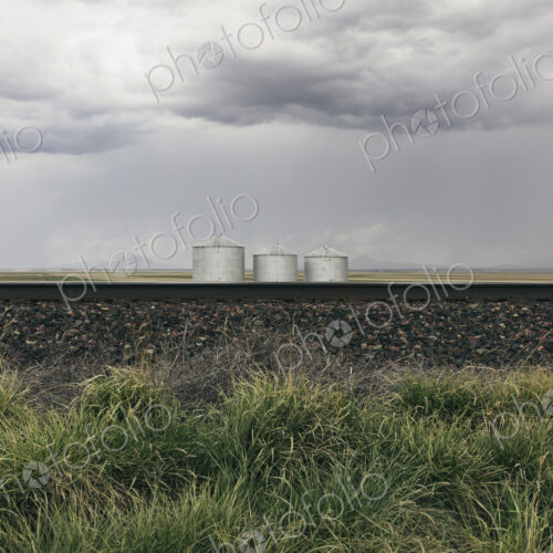 Grain silos and storm clouds over vast farmland and prairie, train tracks in foreground