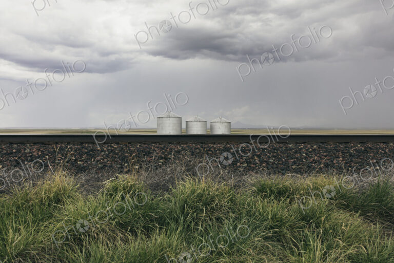 Grain silos and storm clouds over vast farmland and prairie, train tracks in foreground