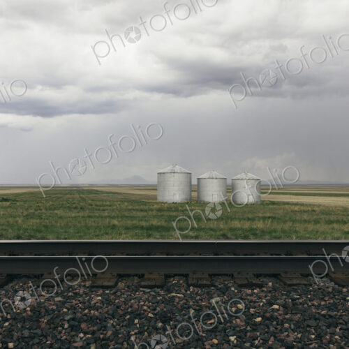 Grain silos and storm clouds over vast farmland and prairie, train tracks in foreground