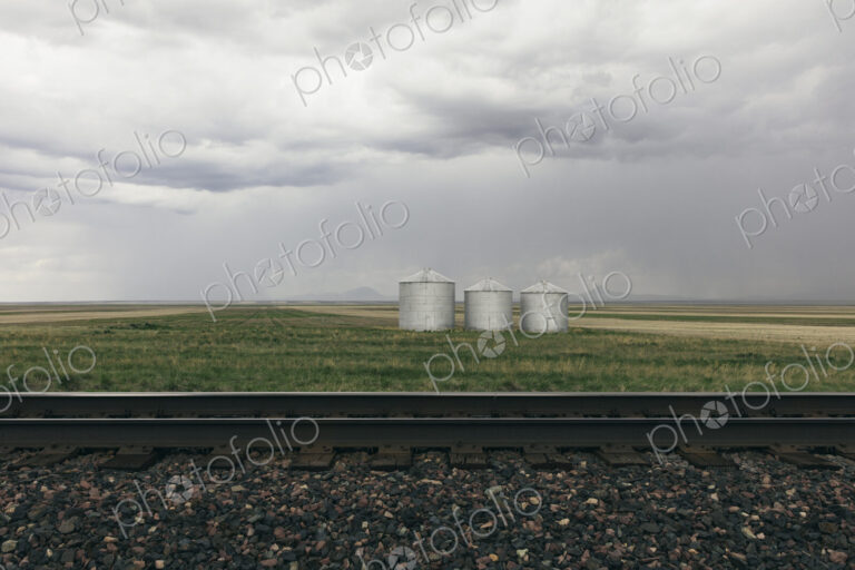 Grain silos and storm clouds over vast farmland and prairie, train tracks in foreground
