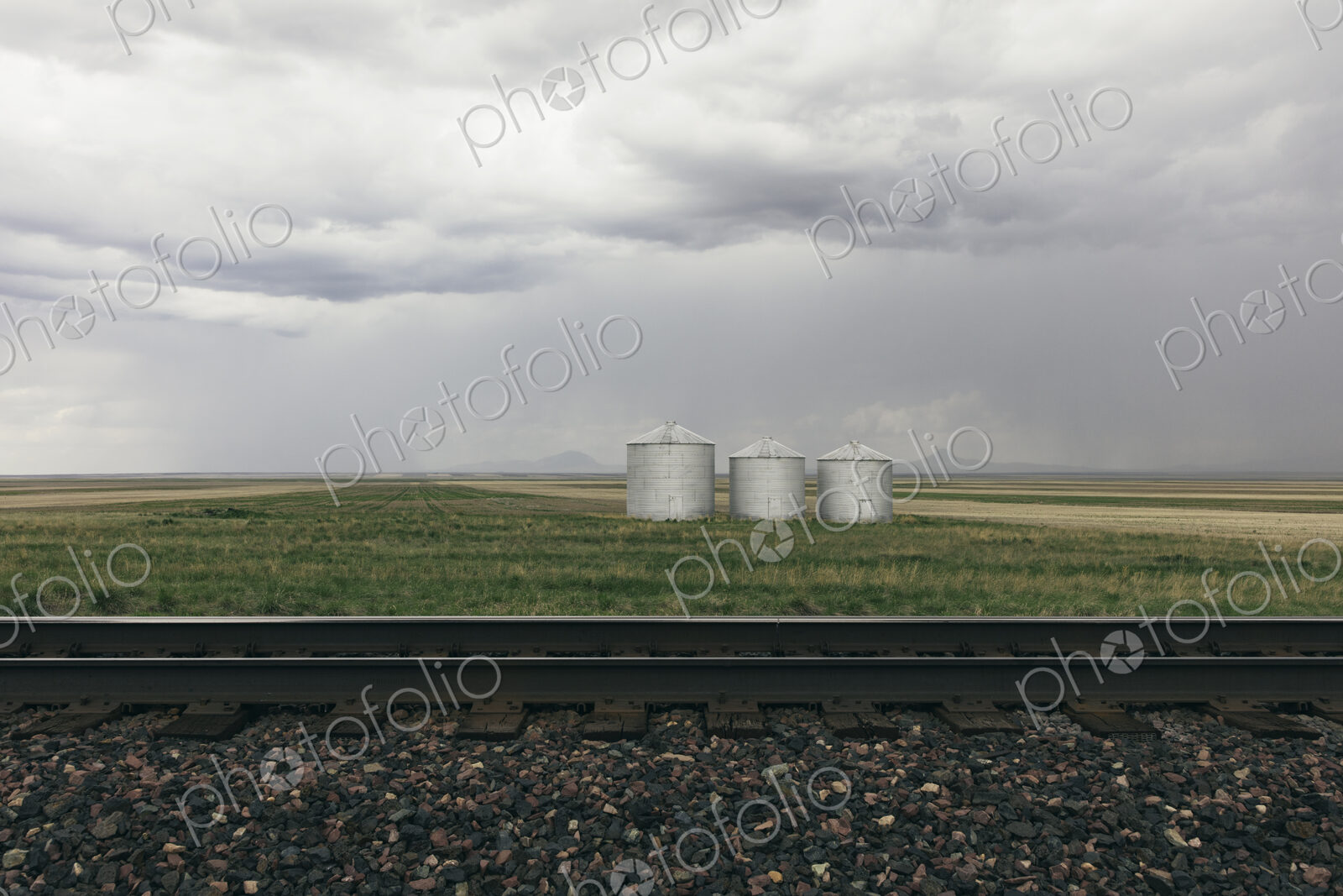Grain silos and storm clouds over vast farmland and prairie, train tracks in foreground
