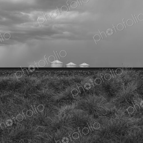 Grain silos and storm clouds over vast farmland and prairie, train tracks in foreground