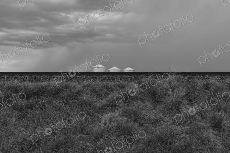 Grain silos and storm clouds over vast farmland and prairie, train tracks in foreground