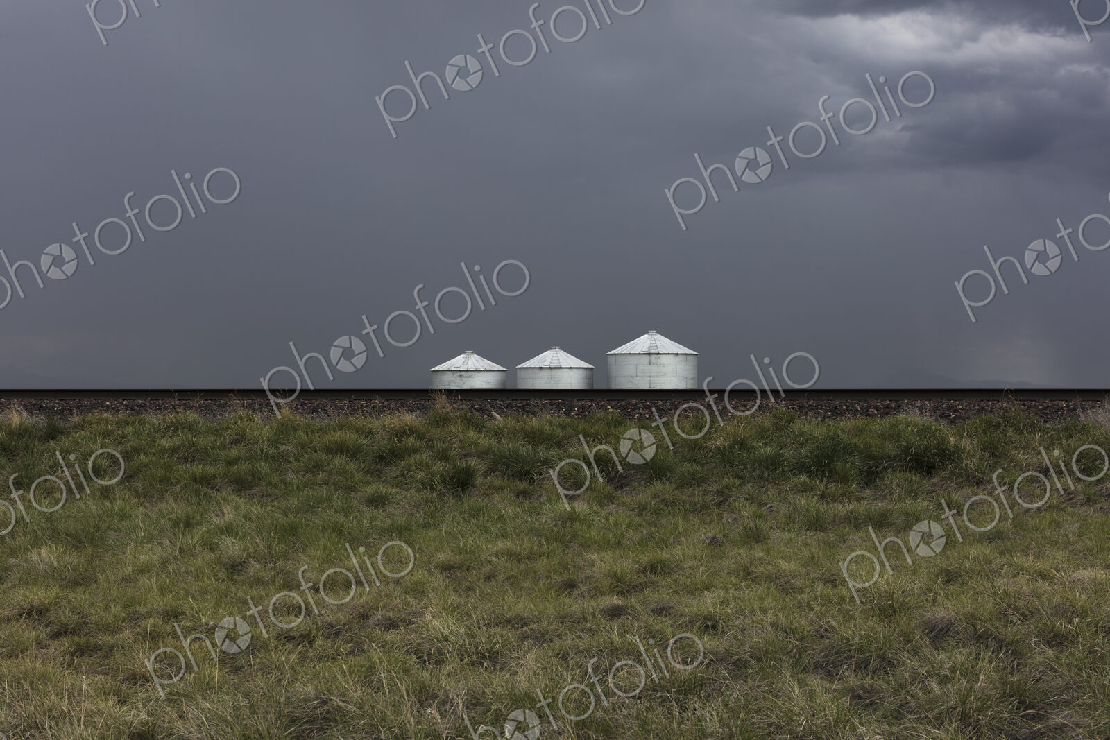 Grain silos and storm clouds over vast farmland and prairie, train tracks in foreground