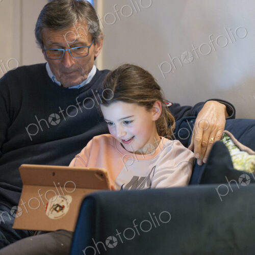 Grandfather and granddaughter sitting together on sofa looking at tablet.