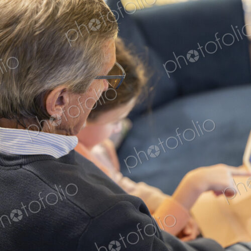 Grandfather and granddaughter sitting together on sofa looking at tablet.