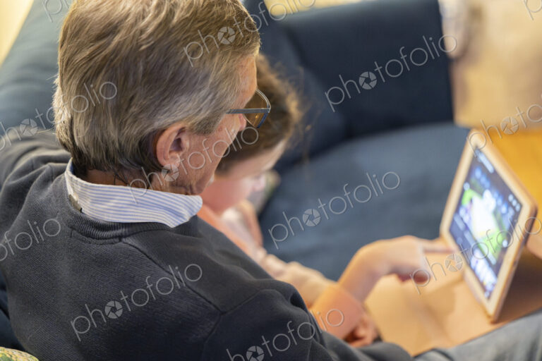 Grandfather and granddaughter sitting together on sofa looking at tablet.
