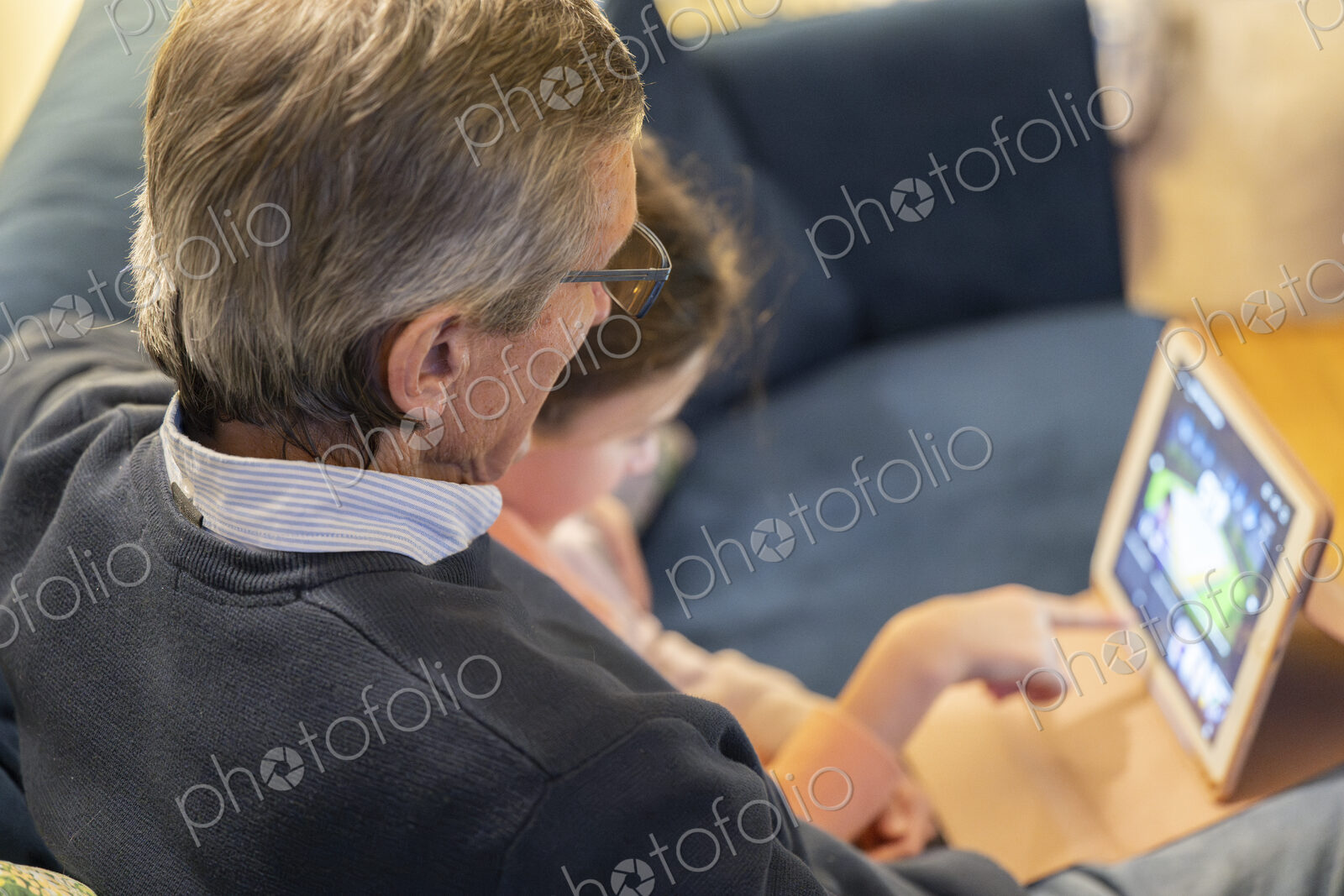 Grandfather and granddaughter sitting together on sofa looking at tablet.