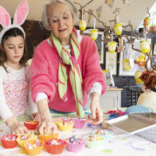 Grandmother and granddaughter making Easter cakes together in kitchen.