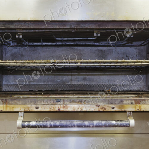 Greasy electric stove oven door open in old catering kitchen.
