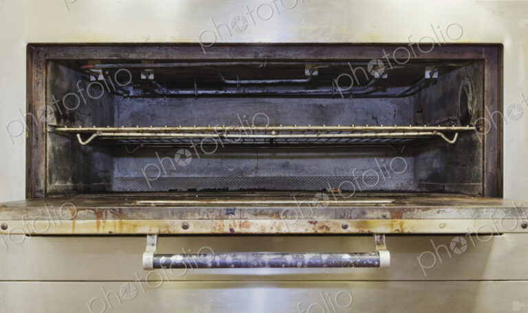 Greasy electric stove oven door open in old catering kitchen.