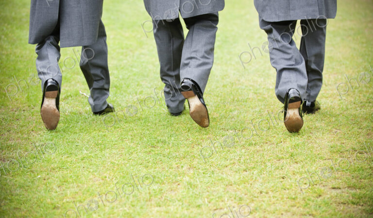 Groom and two best man in black shoes, grey trousers and morning coats walking along a…