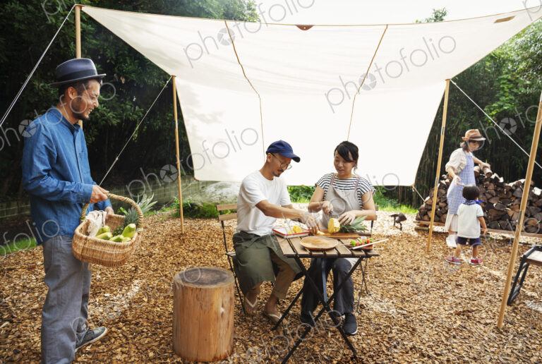 Group of Japanese men and women and boy gathered around a table under a canopy,…