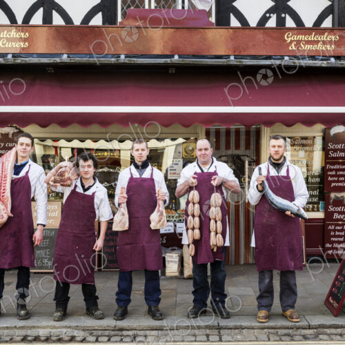 Group of men, butchers and fishmonger, wearing aprons, standing on the pavement…
