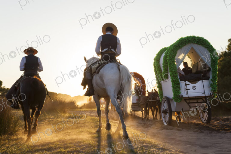 Group of people in horse-drawn wagons and on horseback on a rural dusty road.