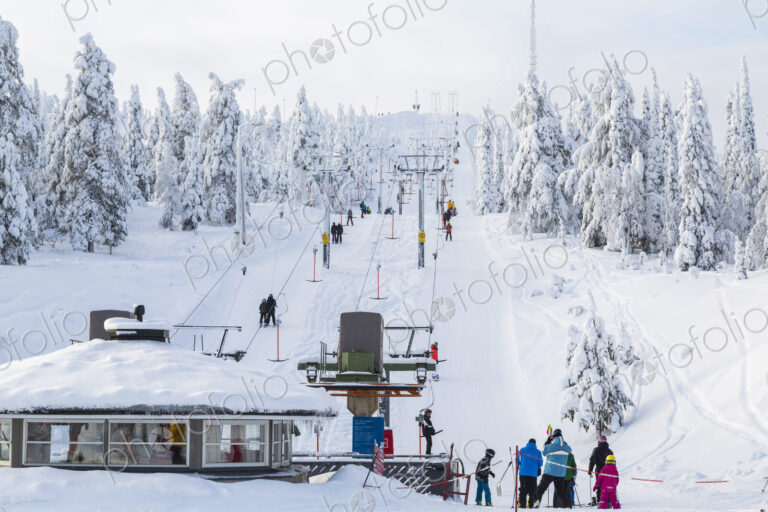 Group of people near a ski lift in forest with snow-covered trees.