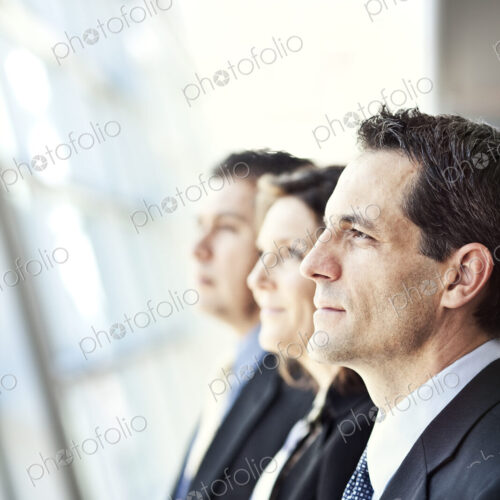 Group of three business people looking out the window of a conference centre lobby.