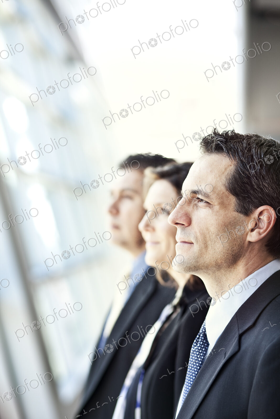 Group of three business people looking out the window of a conference centre lobby.