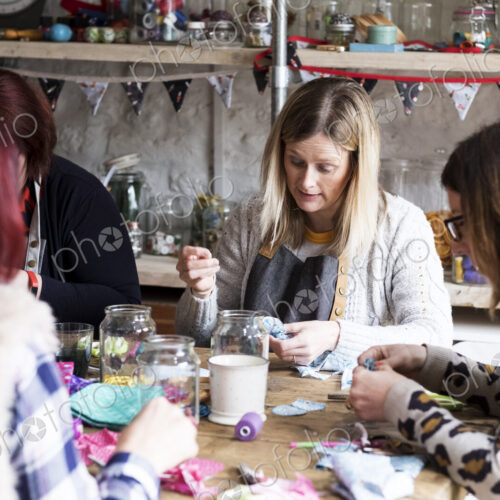 Group of women sitting around a table in a workshop, making fabric flowers.