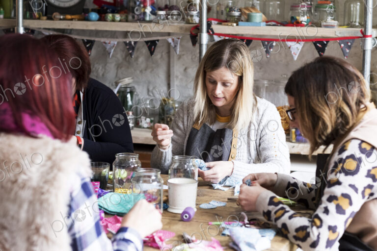Group of women sitting around a table in a workshop, making fabric flowers.