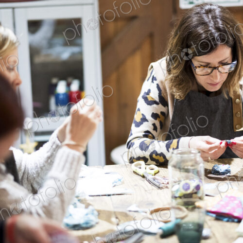 Group of women sitting around a table in a workshop, making fabric flowers.