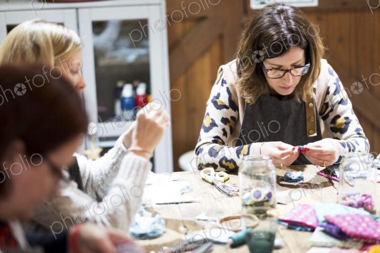 Group of women sitting around a table in a workshop, making fabric flowers.