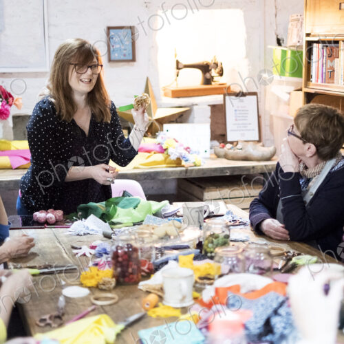 Group of women sitting around a table in a workshop, making fabric flowers.