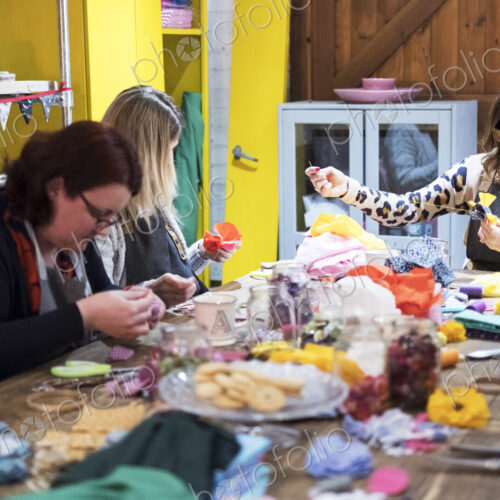 Group of women sitting around a table in a workshop, making fabric flowers.