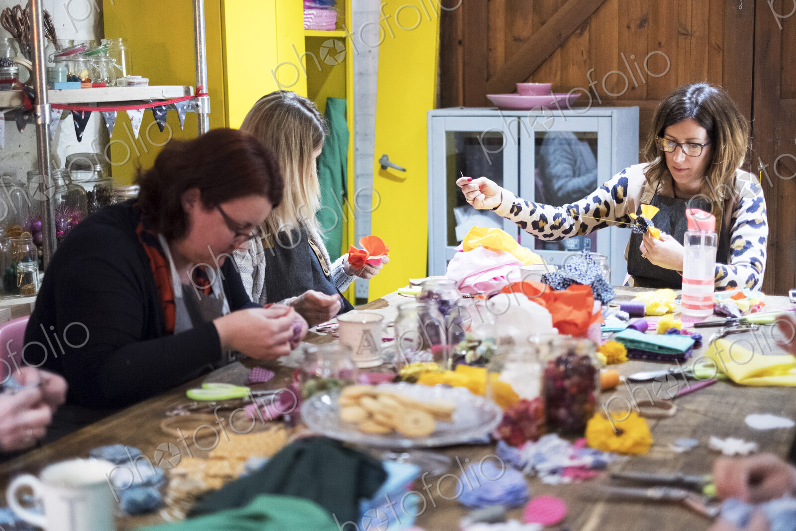 Group of women sitting around a table in a workshop, making fabric flowers.