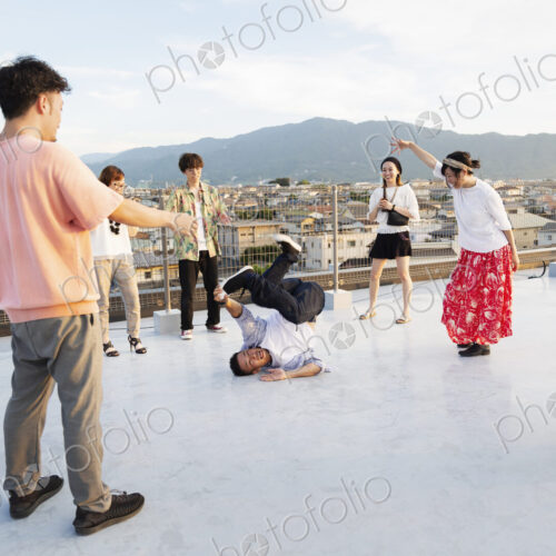 Group of young Japanese men and women dancing on a rooftop in an urban setting. Group of young Japanese men and women dancing on a rooftop in an urban setting.