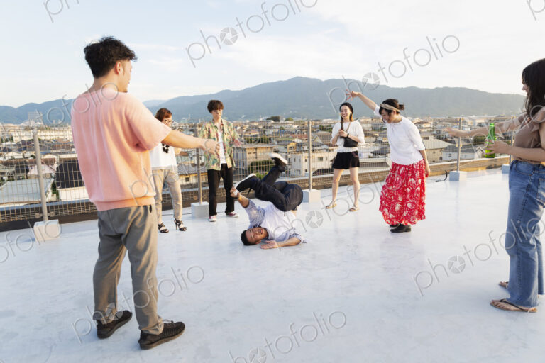 Group of young Japanese men and women dancing on a rooftop in an urban setting.