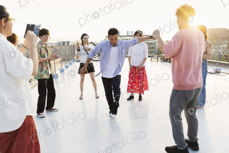 Group of young Japanese men and women dancing on a rooftop in an urban setting.