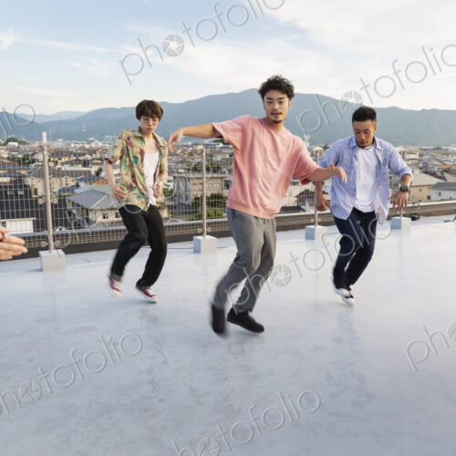 Group of young Japanese men and women dancing on a rooftop in an urban setting. Group of young Japanese men and women dancing on a rooftop in an urban setting.