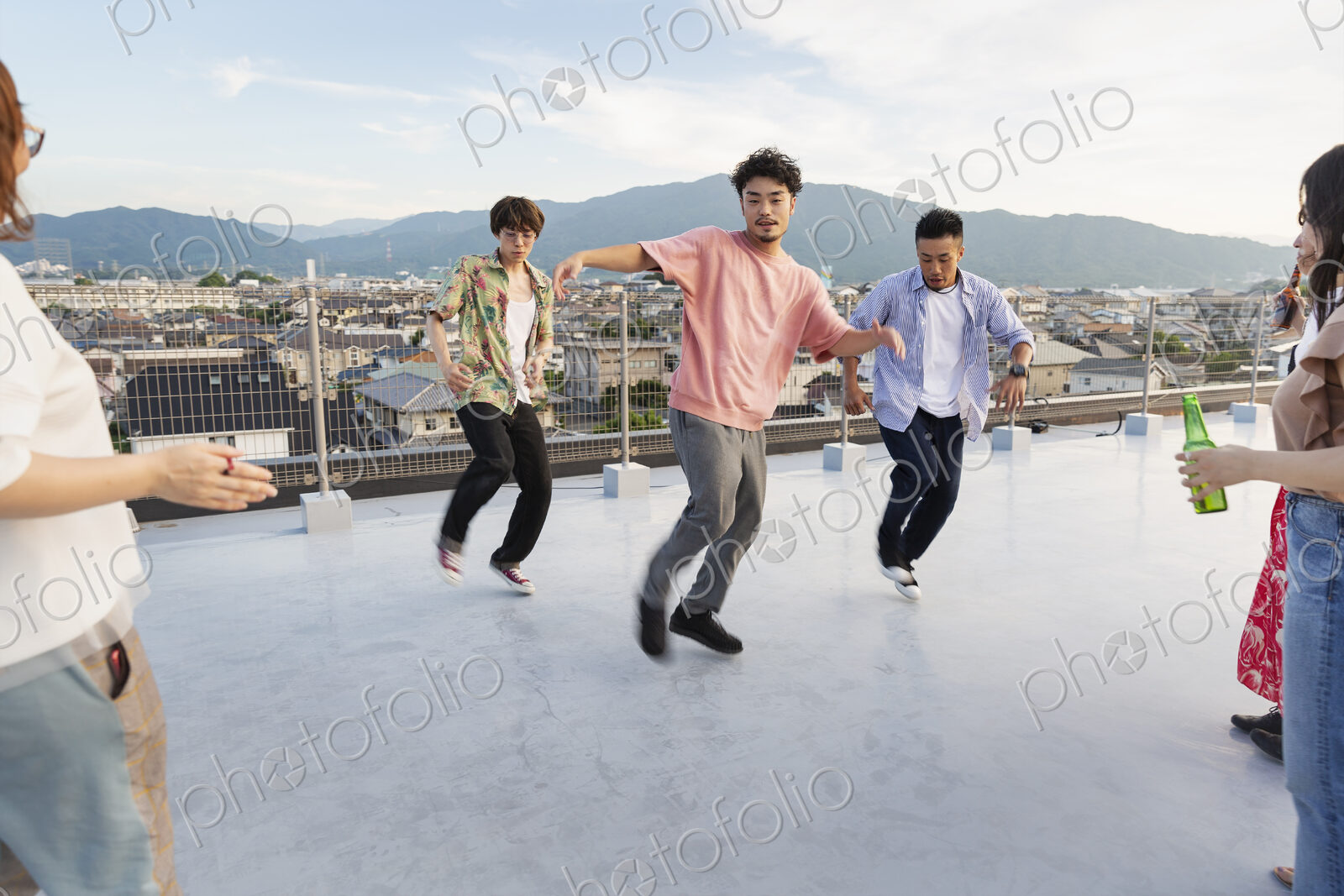 Group of young Japanese men and women dancing on a rooftop in an urban setting.